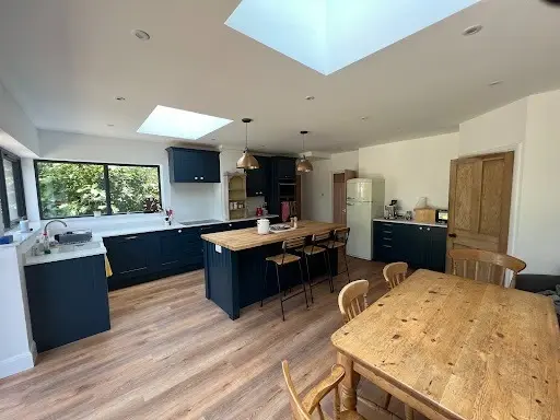 Open-plan kitchen and dining room with a navy island, oak worktop, roof lights and a large picture window