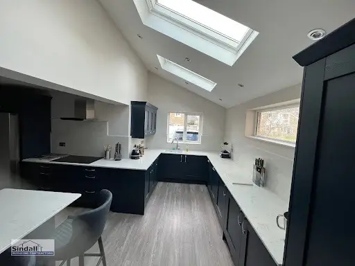 Navy L-shaped kitchen under a vaulted ceiling with roof lights and white worktops