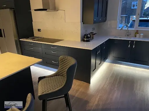 Navy shaker kitchen with pale stone-effect worktops, a chimney extractor and LED plinth lighting