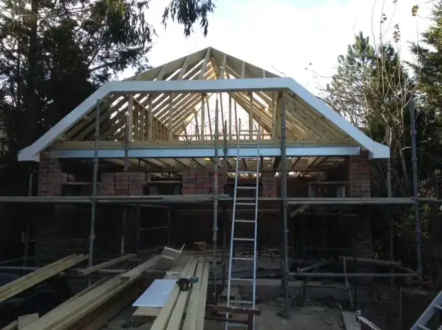 New build house under construction with prefabricated roof trusses craned into position on fresh brickwork, surrounded by scaffolding