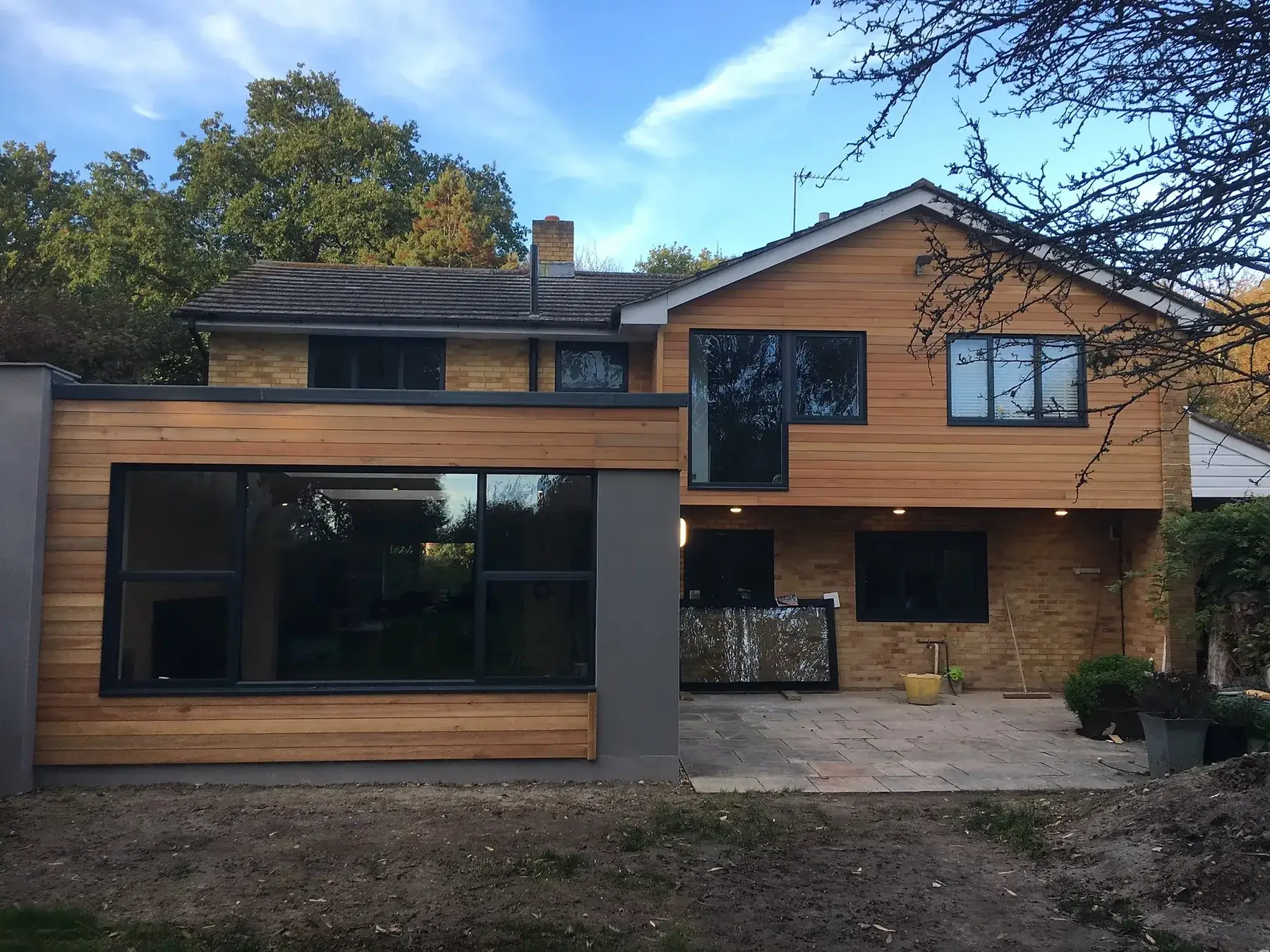 Completed rear extension with cedar cladding, rendered flat-roof section and full-height grey aluminium glazing on a detached house in Mid Sussex