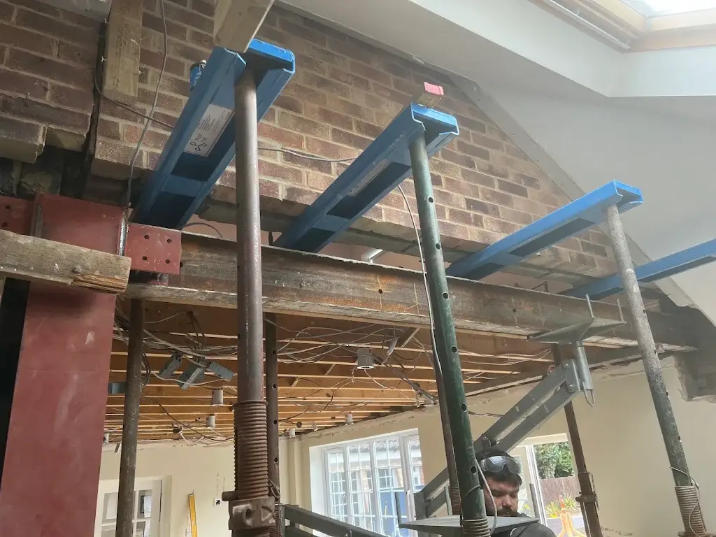 Steel beam bearing onto a padstone with joists propped beneath, inside a house during a structural opening