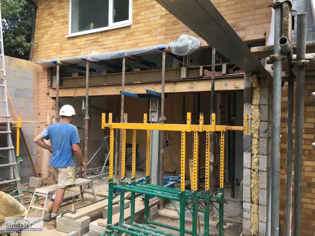 Rear wall of a house needled and propped on Acrow props while a steel beam is lifted into the new opening